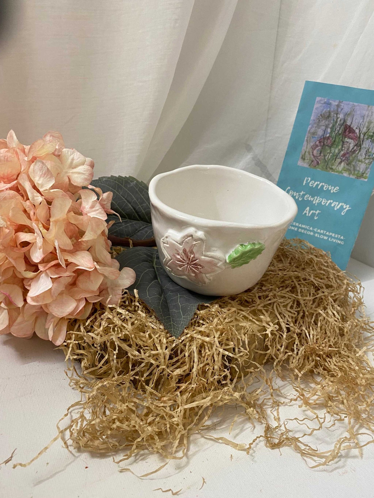White ceramic small bowl with floral decoration from Ciliegio collection placed on natural straw and decorative flowers