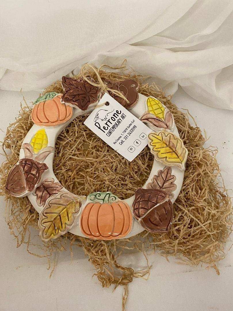 Handmade large white ceramic wreath decorated with autumn leaves, fruits, and pumpkins for seasonal home decor