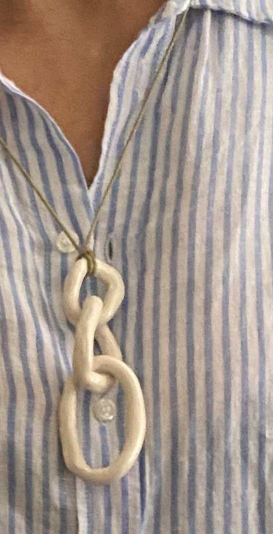 Woman wearing La collana Triple Circle Sand white ceramic necklace with three interlocked circles on striped shirt