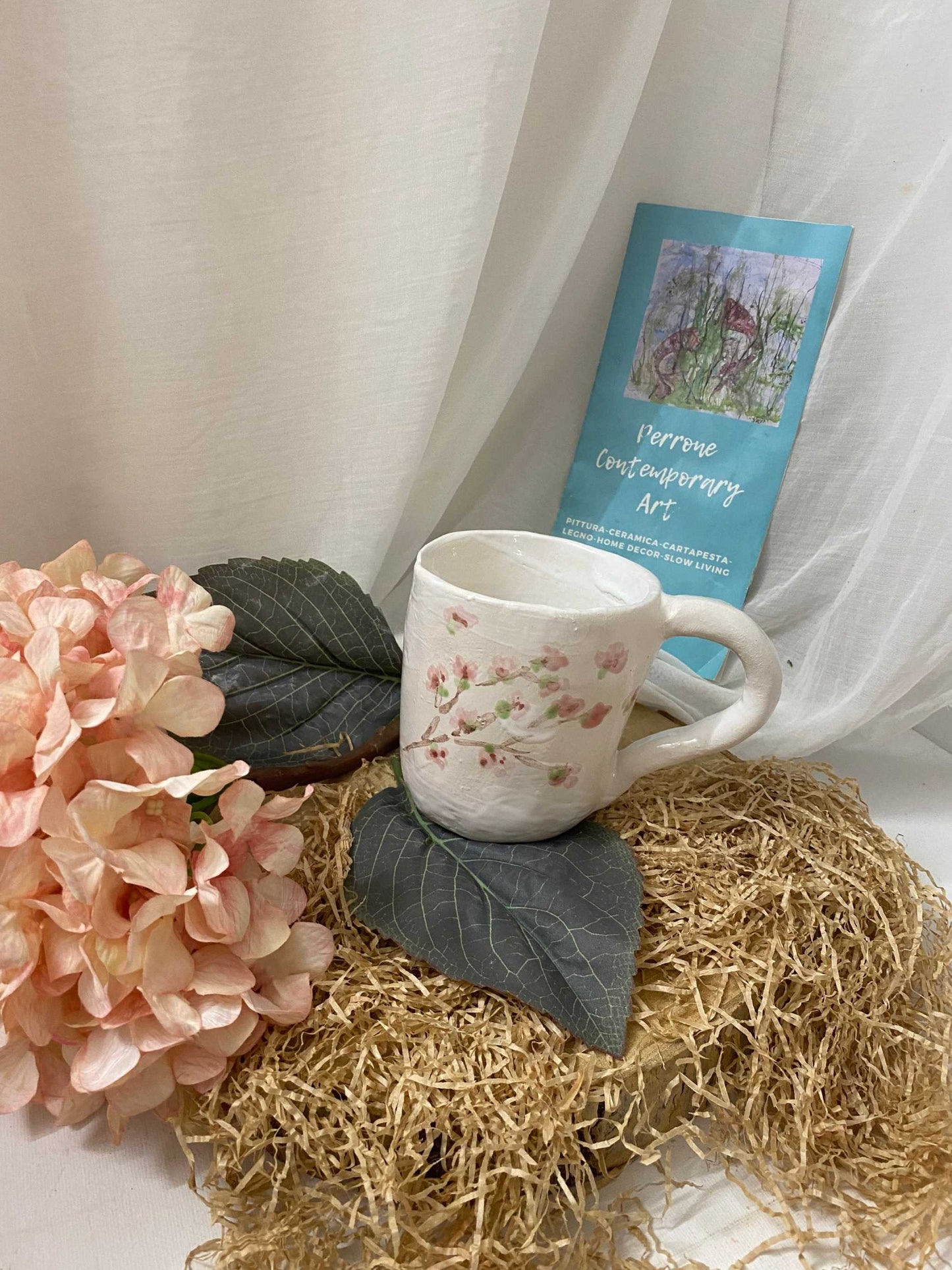 Ceramic Mug Collezione Sakura with delicate pink cherry blossom design and elegant handle on decorative natural fibers.