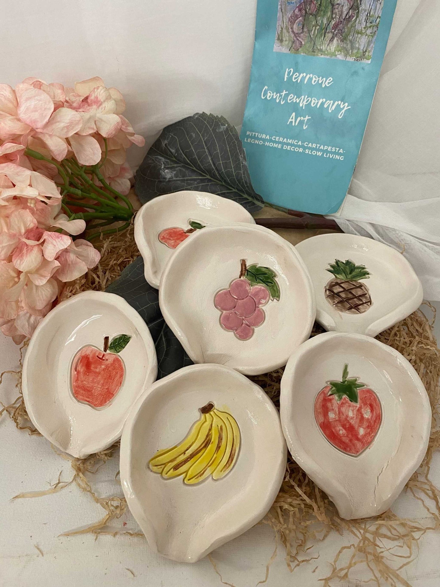 Set of six white ceramic fruit-themed spoon rests with hand-painted apple, grape, pineapple, banana, strawberry, and peach designs