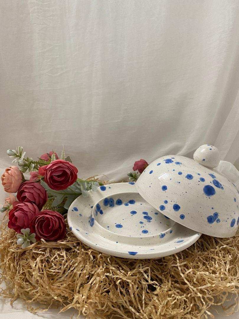 white ceramic butter dish with blue speckles and matching lid on straw mat with red flowers in background porcelain butter keeper container