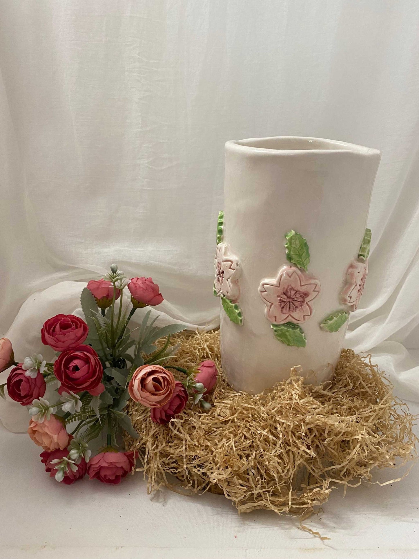 white ceramic flower pot from Ciliegio Collection with pink floral decorations and green leaves on straw base, minimalist and glossy design