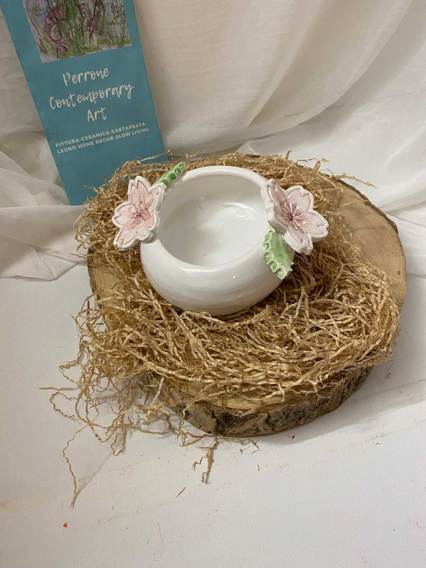 Round white ceramic jewelry box with floral decorations from Ciliegio collection on natural wood and straw display