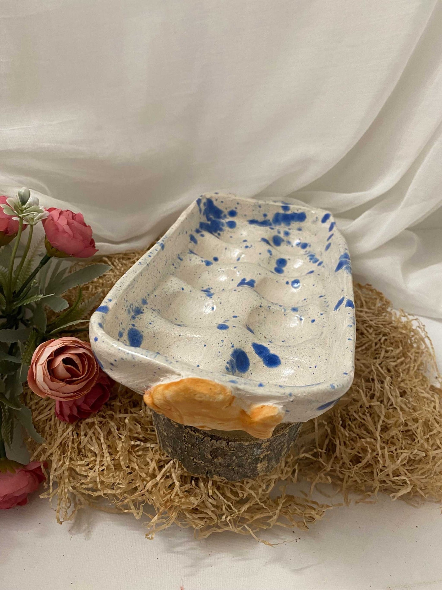 handmade ceramic egg holder with blue speckled design and orange accent on straw mat with flowers