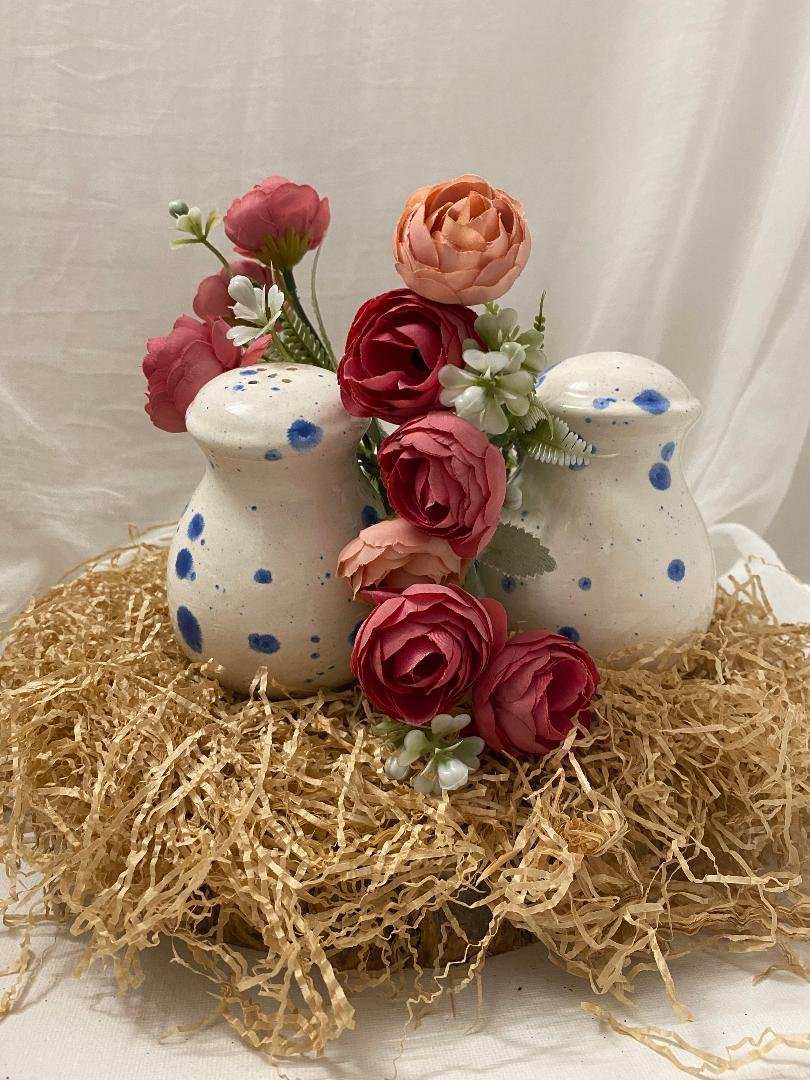 sale e pepe in ceramica bianca with blue spots from Collezione Estate surrounded by decorative flowers on straw bed