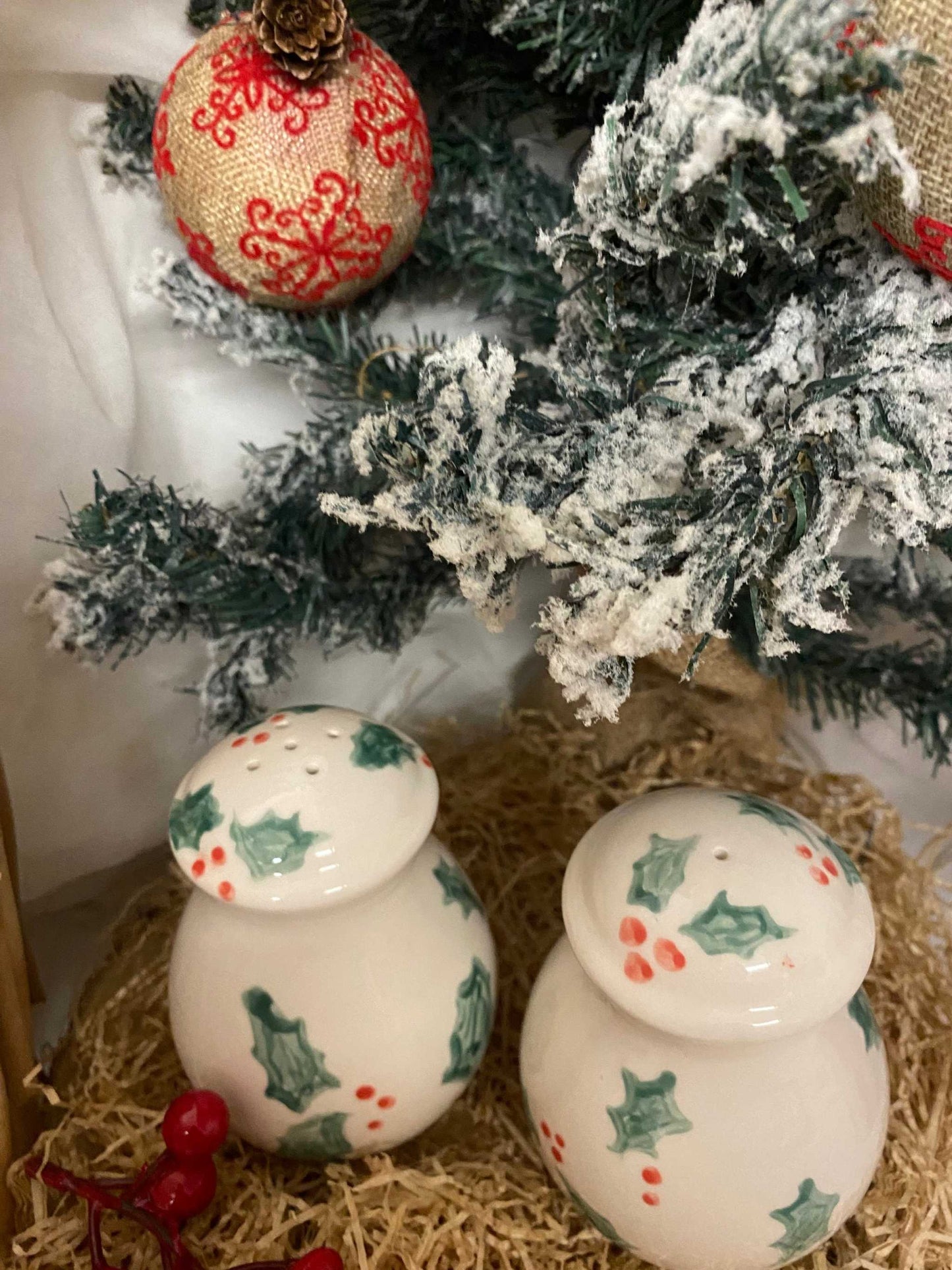 White ceramic salt and pepper shakers with holly berry Christmas design under a decorated snowy tree branch