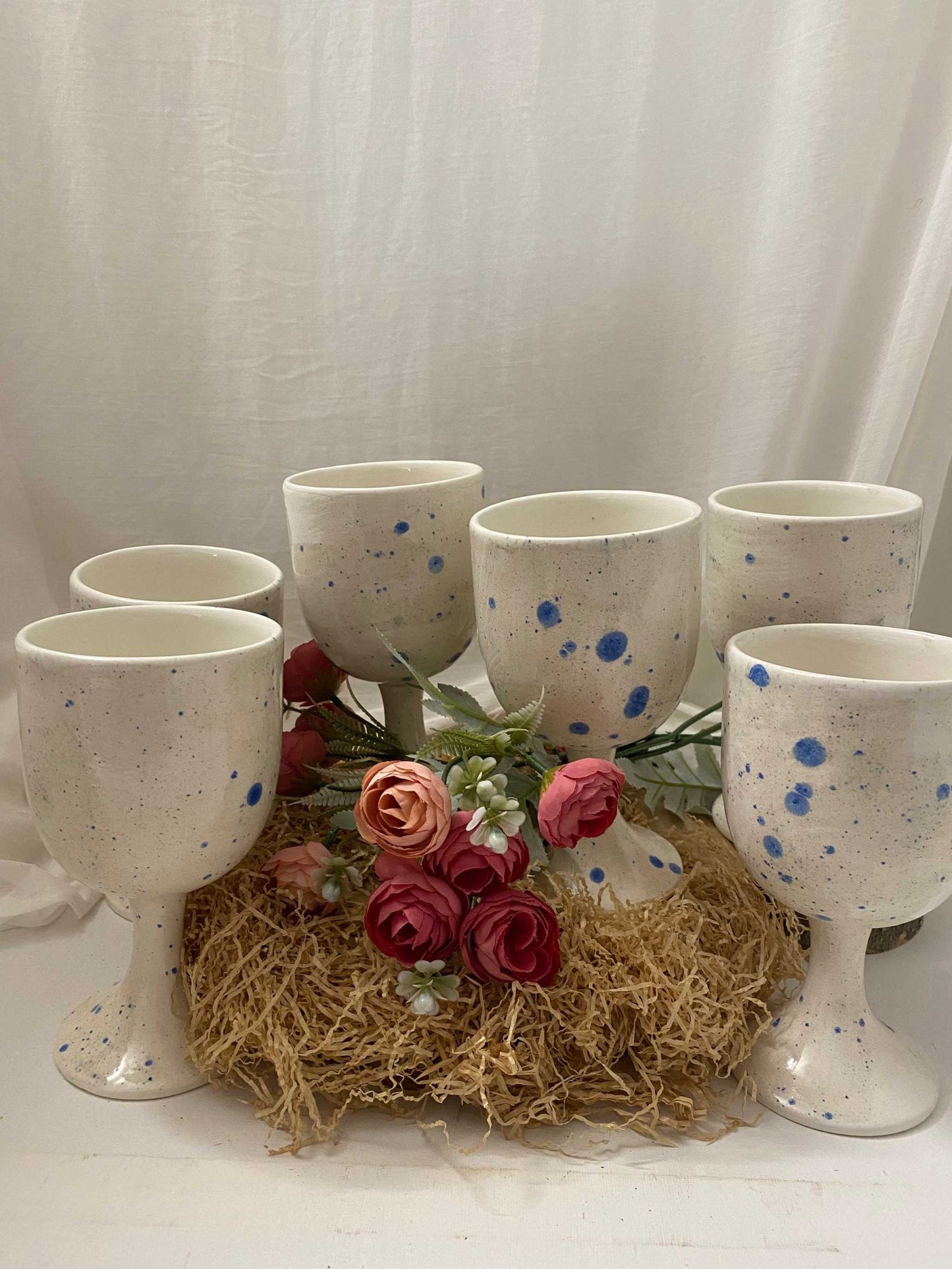 Set of six white ceramic wine glasses with blue speckled design from the Estate Collection, displayed with decorative flowers on a natural straw mat