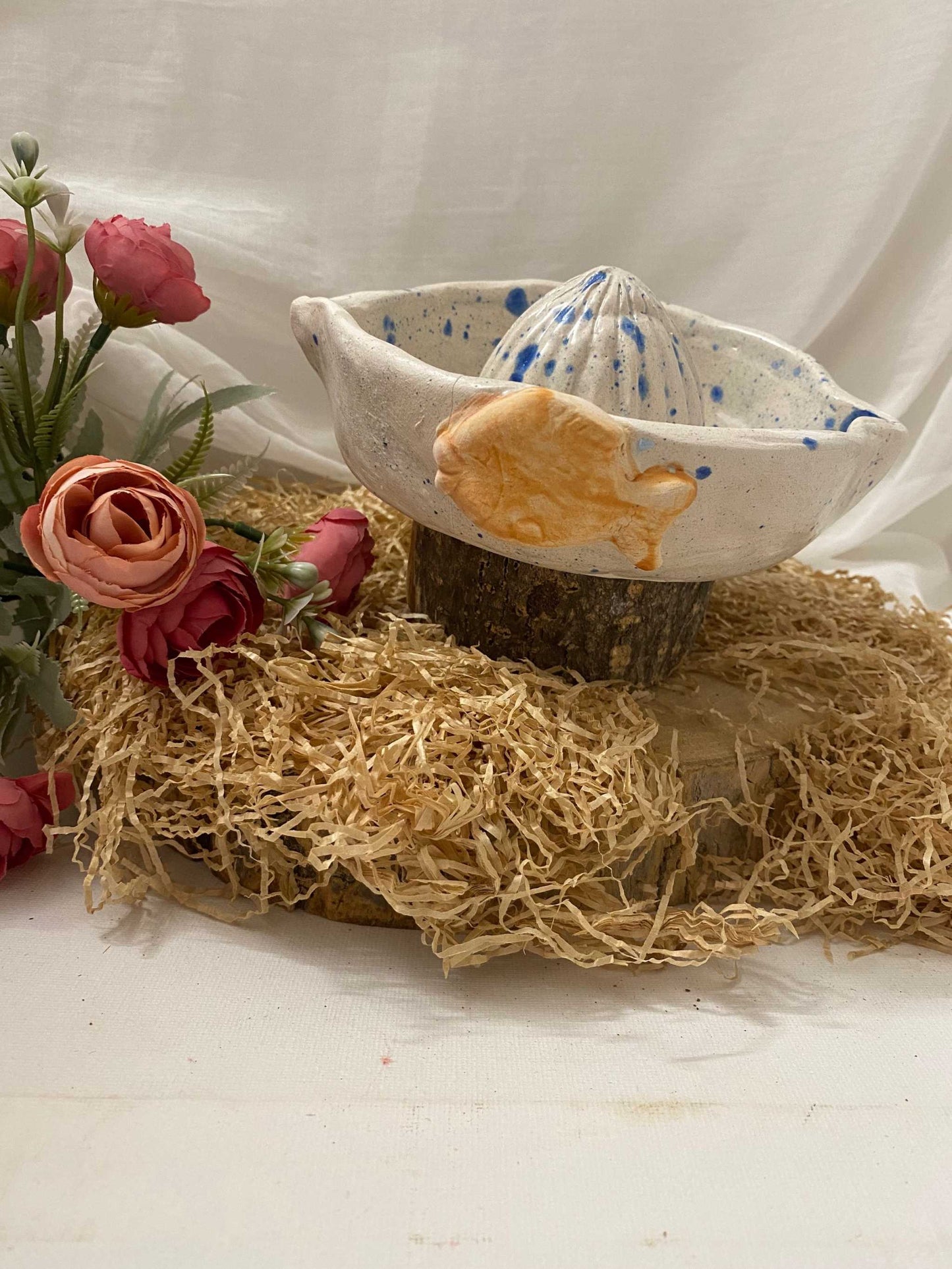 white ceramic citrus juicer with blue speckles and orange fish detail from Estate Collection on rustic straw and wooden base with flowers background