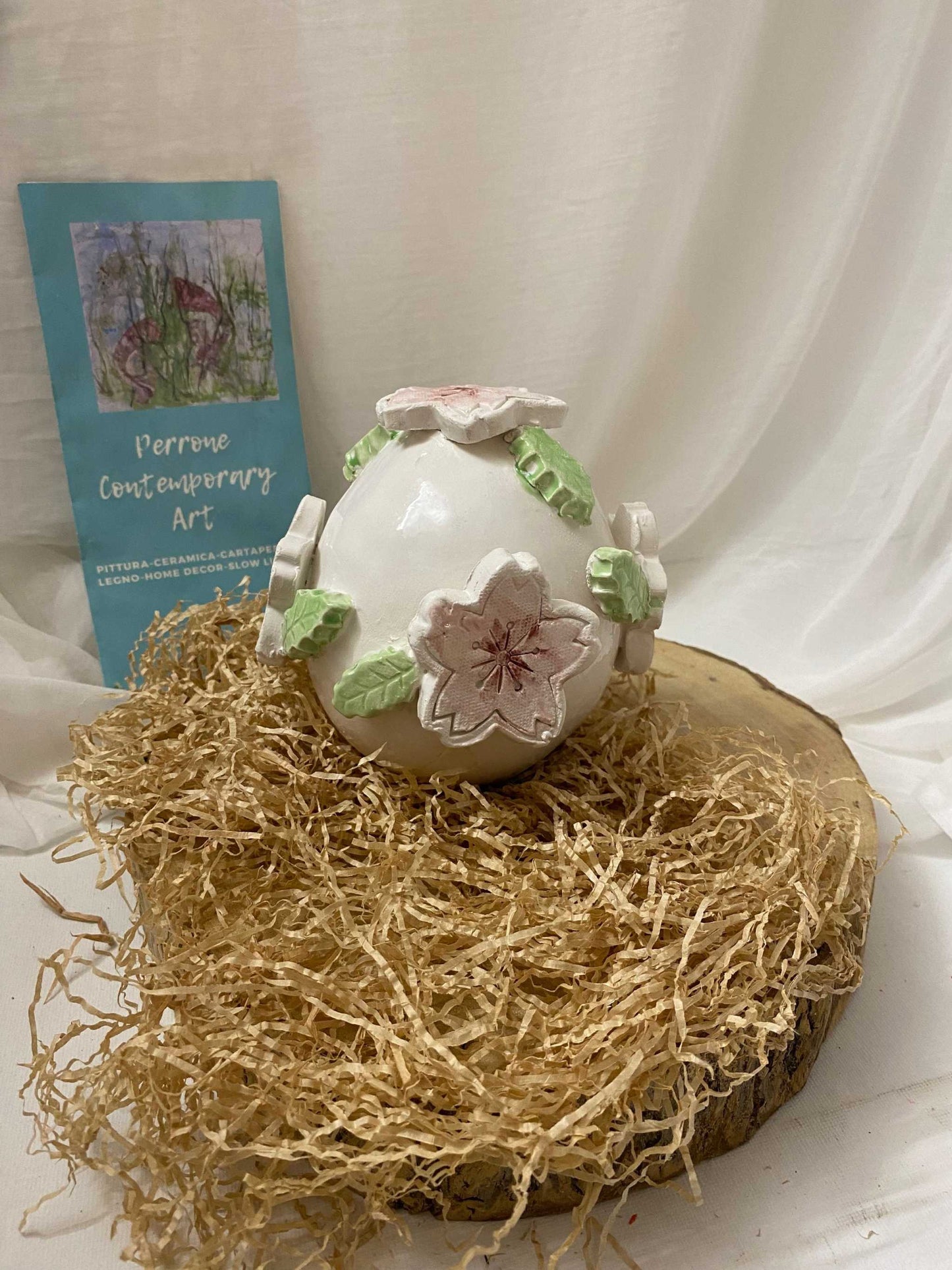 White ceramic decorative egg with pink floral and green leaf accents from Ciliegio Collection, 14 cm tall, elegant home decor on natural straw and wooden base.