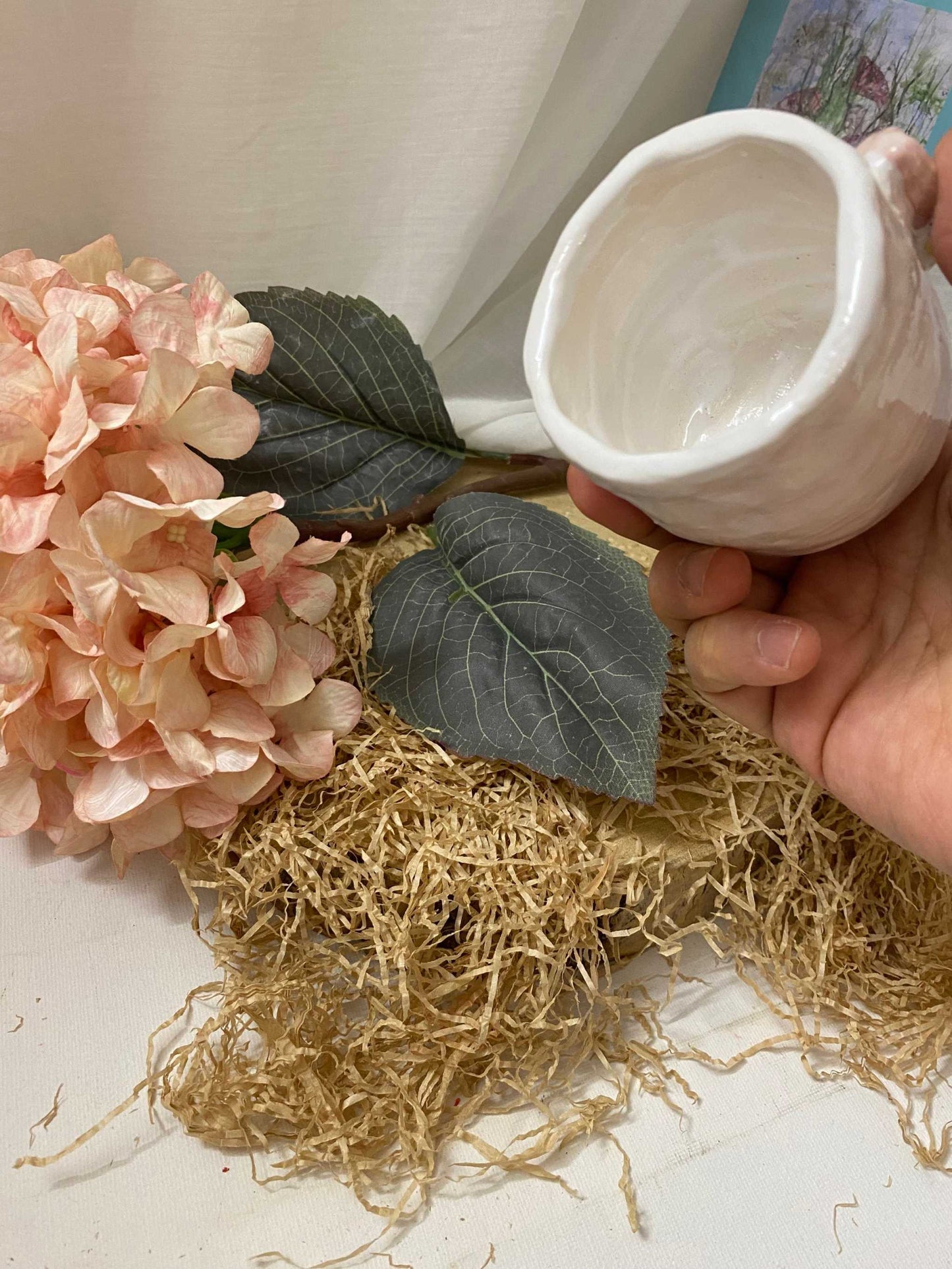 White ceramic Vasetto Butterfly vase held above dried grass and pink hydrangea flowers with green leaves on a white background