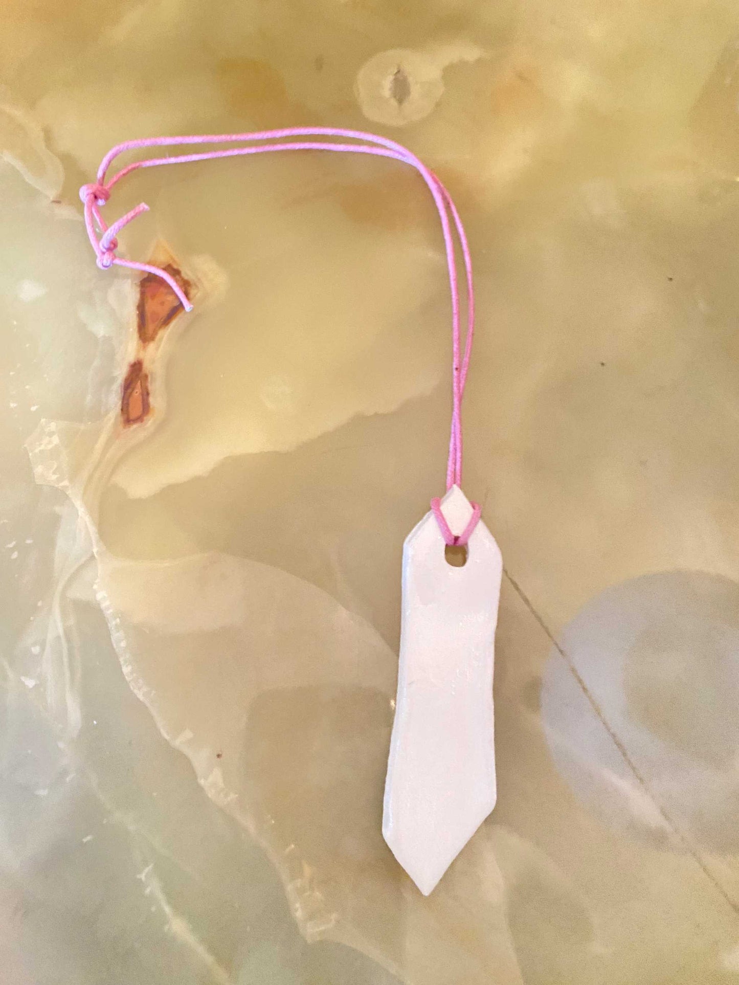 Collana con ciondolo in ceramica bianca e cordino rosa delicato su fondo marmo