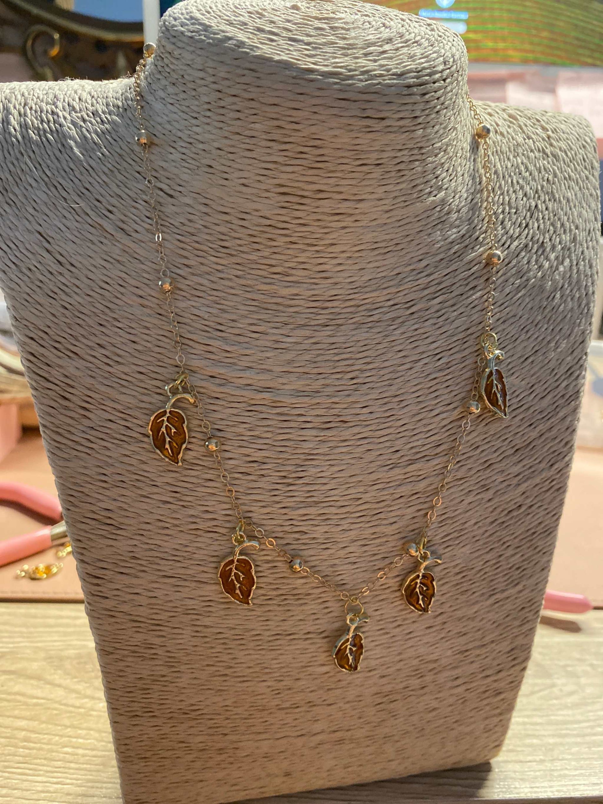 Gold stainless steel leaf necklace from Luxury Bijioux collection displayed on a woven bust