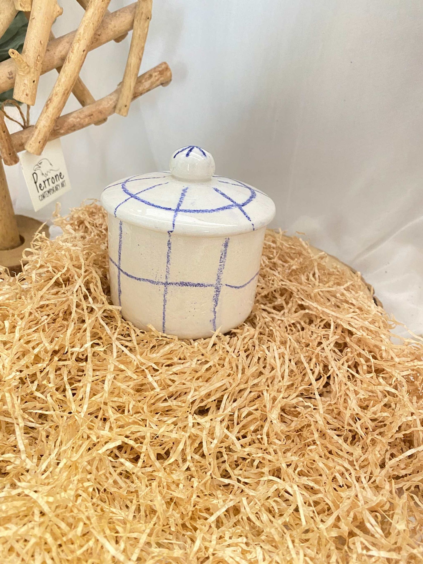 Handmade white ceramic zuccheriera with blue grid pattern and lid, artisanal sugar bowl on straw background