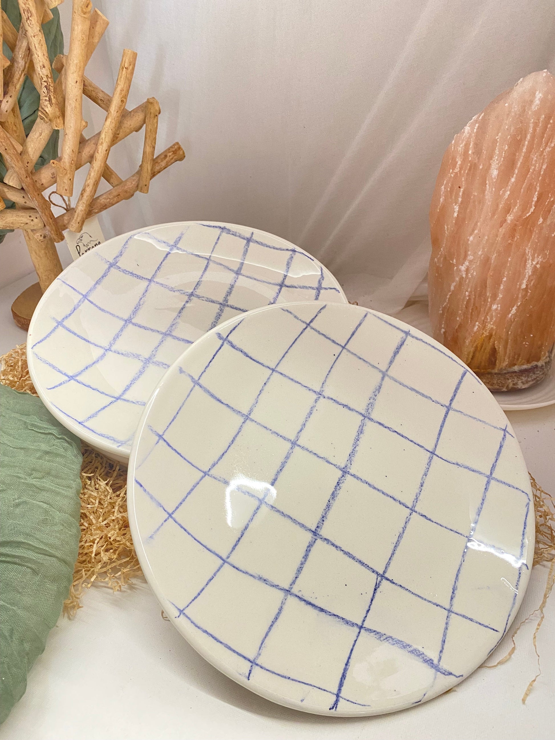 Handmade glazed ceramic plates set with blue grid pattern on white background, artisanal and dishwasher safe.
